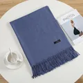Detail of blue cashmere feel scarf with fringe trim and brand tag on a white table - Denim Blue