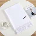 Close-up of white cashmere scarf with fringe details and woven brand label on white desk - Bleached White