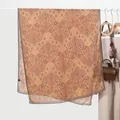 Detail of vintage paisley pattern on large khaki scarf draped on a minimalist hanger - Camel