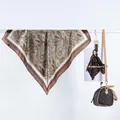 Détail d'un foulard en satin à motif paisley drapé à côté d'un sac à main marron - Paisley Café