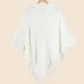 Women's white knitted hooded poncho with fringe trim displayed on a wooden hanger - Hooded Tassel Knit Poncho / White