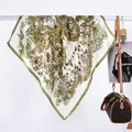 Detail eines Seidenschals mit Schmetterlingsprint, der an einer Stange mit Tasche hängt - Schmetterling Grün