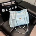 Sac fourre-tout bleu clair avec nœud en dentelle blanche et boucle dorée sur canapé noir - Bleu