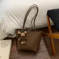 Détail d'un sac cabas marron en cuir avec un pendentif ours en peluche et fines bandoulières - Marron avec Pendentif