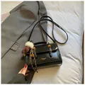 Glänzende schwarze Kuriertasche mit goldener Hardware und Plüsch-Anhänger im Set - Mit Anhänger / Schwarz