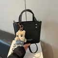 Modische schwarze Handtasche aus Kunstleder mit einem süßen weißen Teddybär-Anhänger - Schwarz