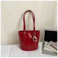 Red glossy bucket bag with cherry pearl charm and slim handles in a modern minimalist setting - Red with Pendant