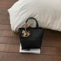 Detail of black pebbled leather bucket bag featuring a unique horse-shaped charm pendant - Black