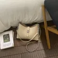 Bolso de hombro beige media luna con cadena plateada y hebilla en suelo de madera - Albaricoque