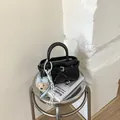 Detail einer schwarzen glänzenden Handtasche mit Schleife und Plüschbär-Anhänger - Schwarz (Mit Bärenanhänger)