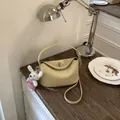 Detailed view of yellow litchi grain leather bag with metal lock on a vintage desk - With Charm / Yellow