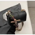 Detail of black cylinder crossbody bag with woven wide strap and plush bunny charm - Black With Pendant