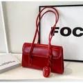 Détail d'un sac à bandoulière rouge vintage avec surpiqûres fines et breloque ovale - Bordeaux