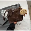 Detailaufnahme der braunen Retro-Umhängetasche mit Schnalle und Plüsch-Anhänger - Kaffeebraun