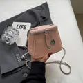 Mini sac seau rose texturé avec bandoulière chaîne et breloque camélia tenu à la main - Rose