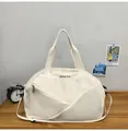 Vista detallada de la bolsa de viaje crema con logo negro y correa sobre un escritorio - Blanco