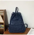 Detailed close-up of dark blue denim drawstring backpack on a wooden table setup - Dark Blue