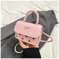 Detailed macro view of pink polka dot crossbody bag with silver bow accent on gray suit - Pink