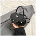 Mini black crossbody bag with white polka dots and silver bow detail in hand - Black
