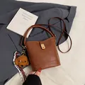 Brown leather bucket bag with top handle and plush puppy charm in minimalist design - With Pendant / Brown