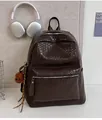 Detail eines dunkelbraunen Rucksacks mit Webstruktur, Bärenanhänger und Kopfhörern - Braun mit Anhänger