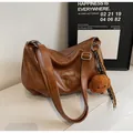 Brown faux leather crescent shoulder bag with plush teddy bear pendant on white marble - Yellow Brown