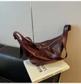 Close-up of a burgundy oil leather crescent bag with pleated detail on a business book - Burgundy