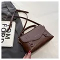 Detail view of a dark brown crossbody bag with flap cover and elegant gold branding - Brown