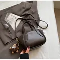 Dark brown leather bucket bag with plush charm on a grey blazer background - Coffee