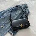 Minimalist black leather underarm bag with gold horseshoe buckle on denim jacket - Black