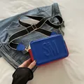 Bolso bandolera cuadrado azul y rojo con correa ancha sobre chaqueta vaquera - Azul