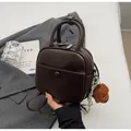 Detail eines dunkelbraunen Mini-Lederrucksacks mit Bärenanhänger auf grauem Blazer - Kaffee Mit Kaninchenanhänger