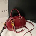Sac Boston en cuir verni rouge foncé avec détails dorés et pendentif décoratif - Rouge avec pendentif