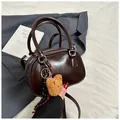 Detail of dark brown glossy leather handbag featuring a cute plush bear charm on the zipper - Coffee