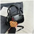 Glossy black faux leather handbag with brown plush bear charm and slender shoulder strap - Black