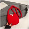 Gros plan d'un sac à bandoulière en peluche rouge avec un pompon blanc sur laine grise - Rouge