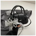 Detail of black Boston bag with glossy finish and decorative pearl bow on a grey blazer - With Ornament / Black
