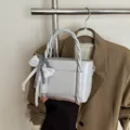Light gray bucket bag with checkered bow and lace detail on a blazer backdrop - Gray