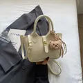 Bolso saco beige minimalista con textura cocodrilo y colgante de osito suave - Blanco Roto