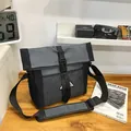 Grau-schwarze Kurier-Umhängetasche mit Netztasche und Schnalle auf einem Holztisch - Schultertasche / Schwarz