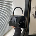 Elegante bolso de charol negro con herrajes dorados y solapa de diseño triangular - Negro