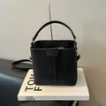 Matte black bucket bag with vertical stitching and top handle on a white display stand - Black (Without Charm)
