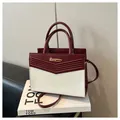 Elegante bolso de mano en contraste rojo y blanco con logo dorado sobre un libro - Burdeos