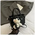 Close-up of black patent leather handbag with belt buckle and cute plush puppy charm - Black with Pendant