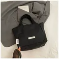 Detail of minimalist black nylon tote bag with white woven label on neutral background - Black