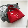 Detail view of large red canvas tote bag with white embroidery on a casual lifestyle background - Red