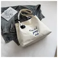 Detail of off-white canvas tote bag with blue embroidery and leather tag on the handle - White