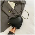 Chic black heart-shaped crossbody bag with gold chain strap on grey suit - Black