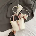 Borsa a secchiello beige con manici rosa e ciondolo a forma di orso su sfondo minimalista - Bianco