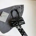 Schicke schwarze Handtasche mit großer Nietenschleife und Glanzoptik auf grauem Anzug - Schwarz